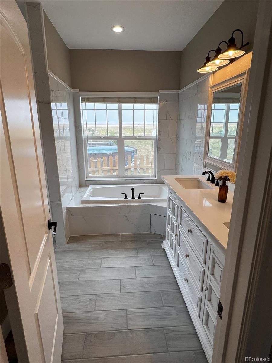 6945 Strasburg Road Strasburg, CO 80136 - Photo 19 of 42 a bathroom with a double vanity sink a mirror and a bathtub