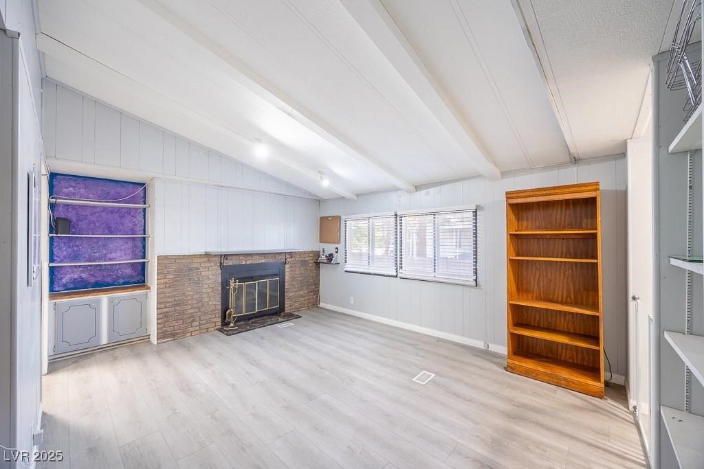 1208 Inca Lane Henderson, NV 89015 - Photo 16 of 21 Unfurnished living room featuring light wood finished floors, a brick fireplace, and wood walls