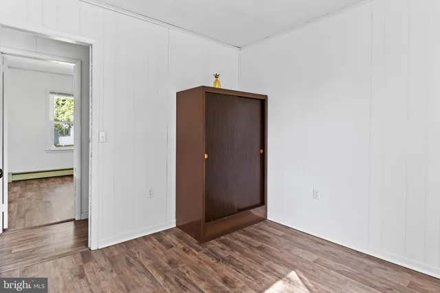 a view of an empty room with wooden floor and a hallway
