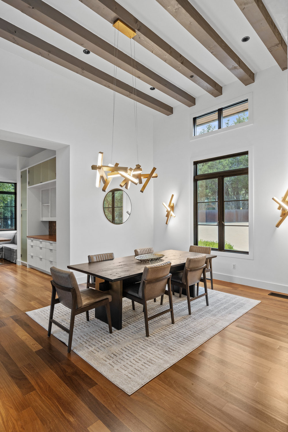 1905 Paisano Road Austin, TX 78746 - Photo 7 of 40 A striking chandelier illuminates the dining area, featuring an impressive beamed ceiling and elegant wood flooring.