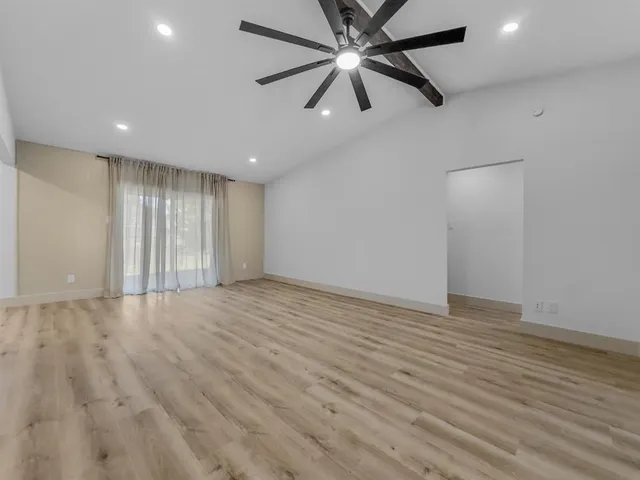 an empty room with wooden floor fan and windows