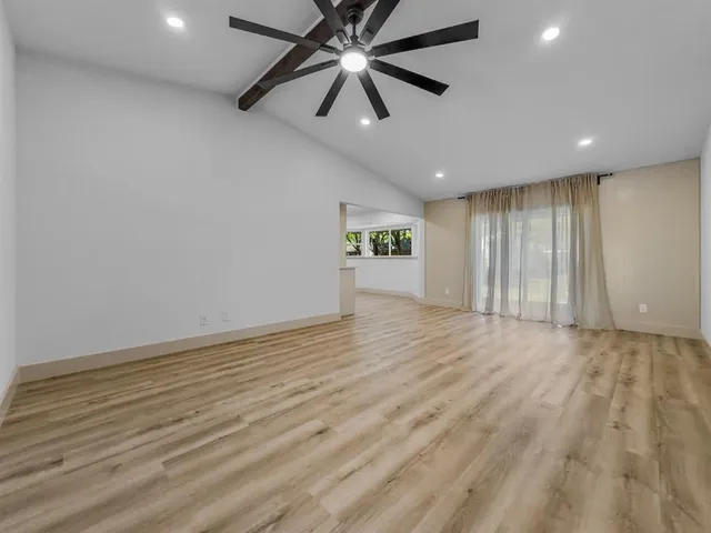 an empty room with wooden floor ceiling fan and windows