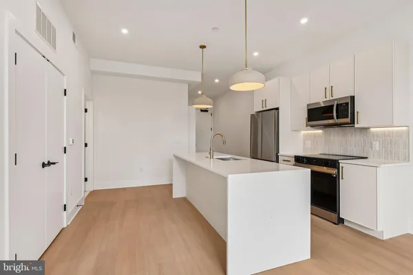 a kitchen with stainless steel appliances a sink a refrigerator a center island a stove and a wooden floors