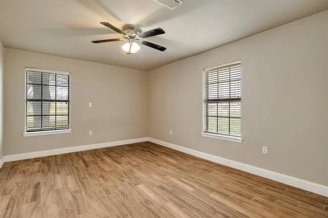 an empty room with wooden floor chandelier fan and windows