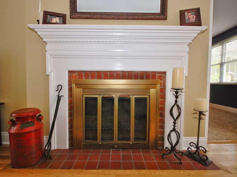 Other. A close-up view of the wood-burning fireplace in the living room, featuring brick surround, corniced wooden mantle, and tile hearth. Coziness defined.