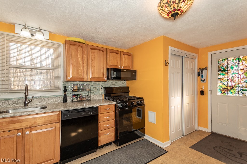 Kitchen featuring a textured ceiling, backsplash, sink, black appliances, and light tile floors
