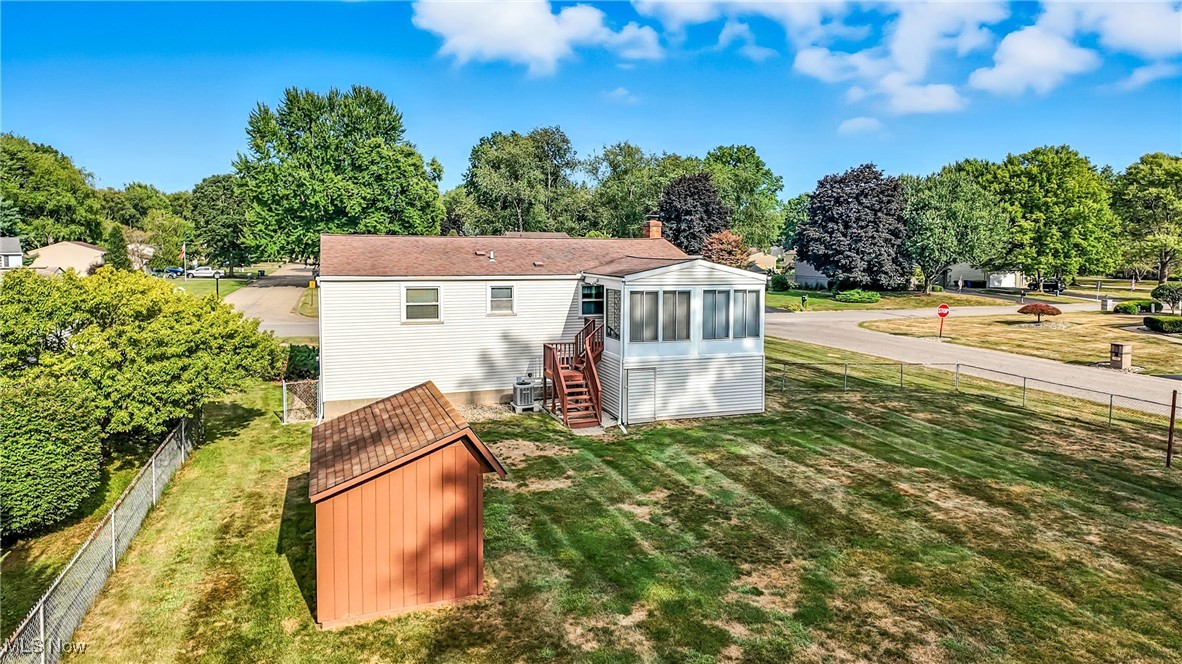 7797 Raglan Drive Northeast Warren, OH 44484 - Photo 12 of 50 Back of property with a fenced backyard, a sunroom, view of scattered trees, stairway, and a storage unit