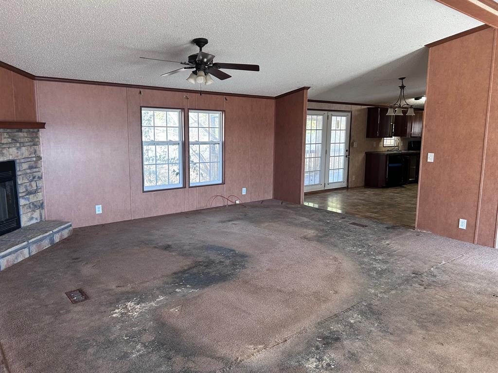 329 Canvas Back Drive Princeton, LA 71067 - Photo 7 of 20 Unfurnished living room with a stone fireplace, crown molding, healthy amount of natural light, a ceiling fan, and wood walls