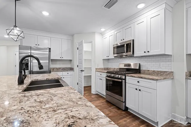 a kitchen with stainless steel appliances granite countertop a sink a stove and a wooden floors