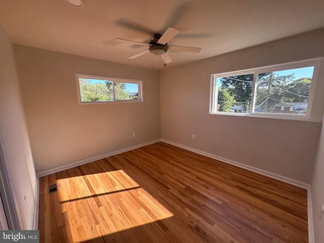 an empty room with wooden floor fan and windows