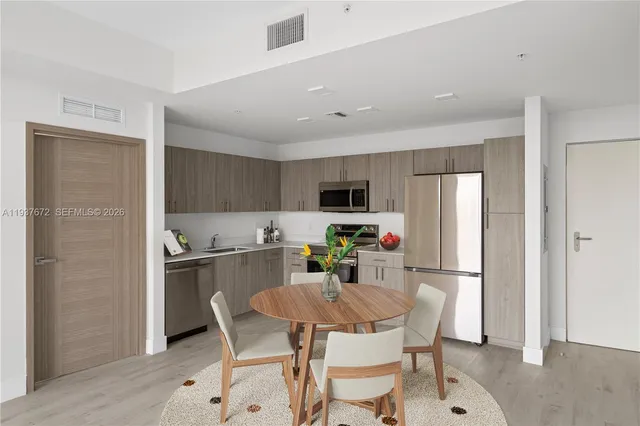 a kitchen with stainless steel appliances a dining table chairs refrigerator and microwave