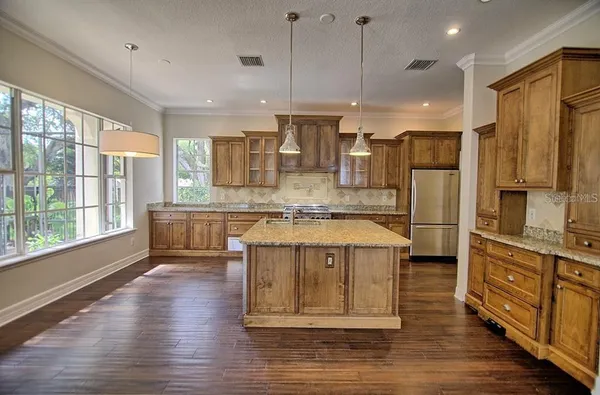 a large kitchen with stainless steel appliances granite countertop a refrigerator a oven a island and a stove with wooden floors