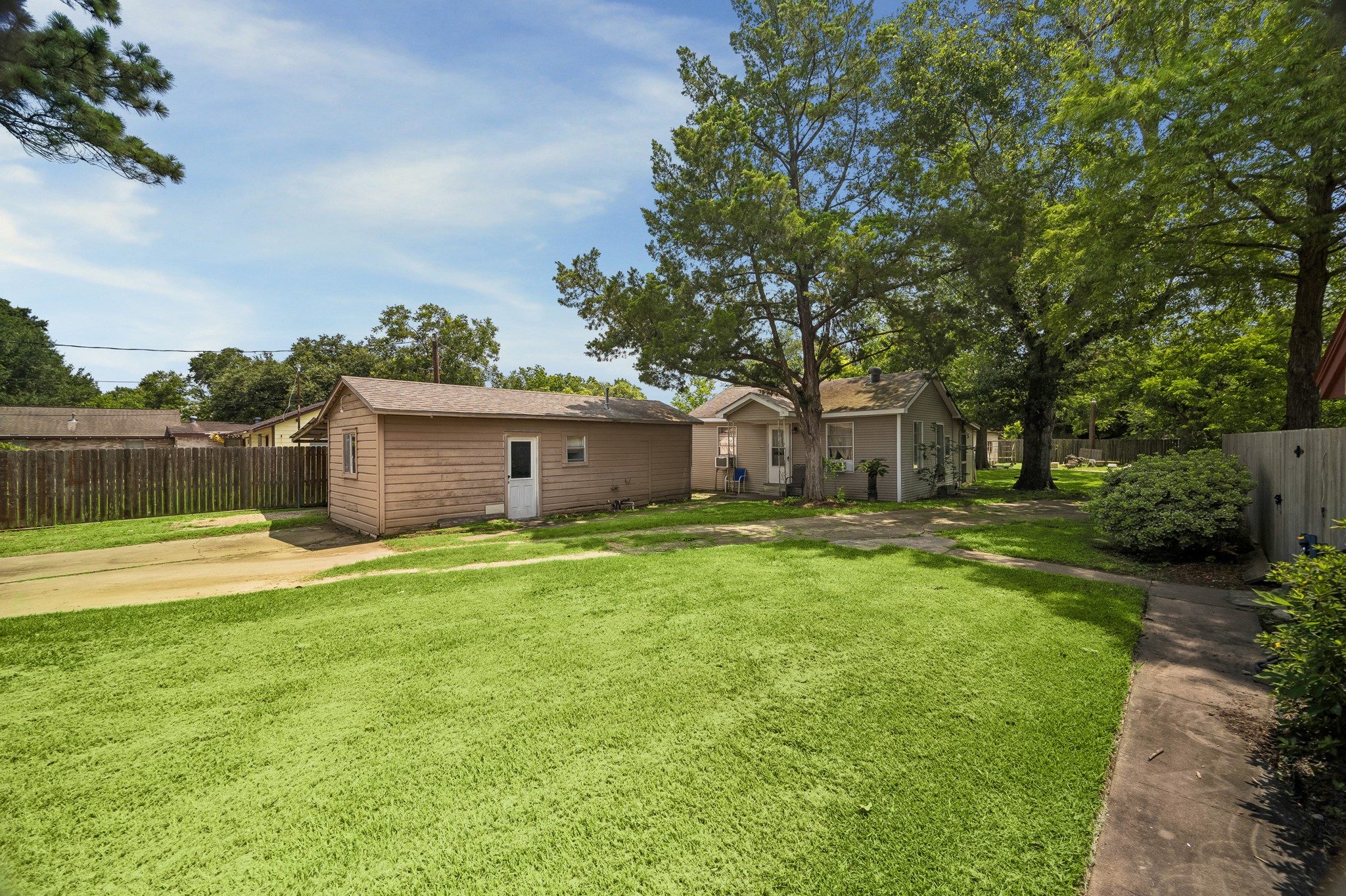 413 Mebane Lane Rosenberg, TX 77471 - Photo 26 of 30 This photo showcases a cozy backyard with lush green grass and mature trees. The small house and detached storage building with a detached carport surrounded by lush green grass and mature trees.