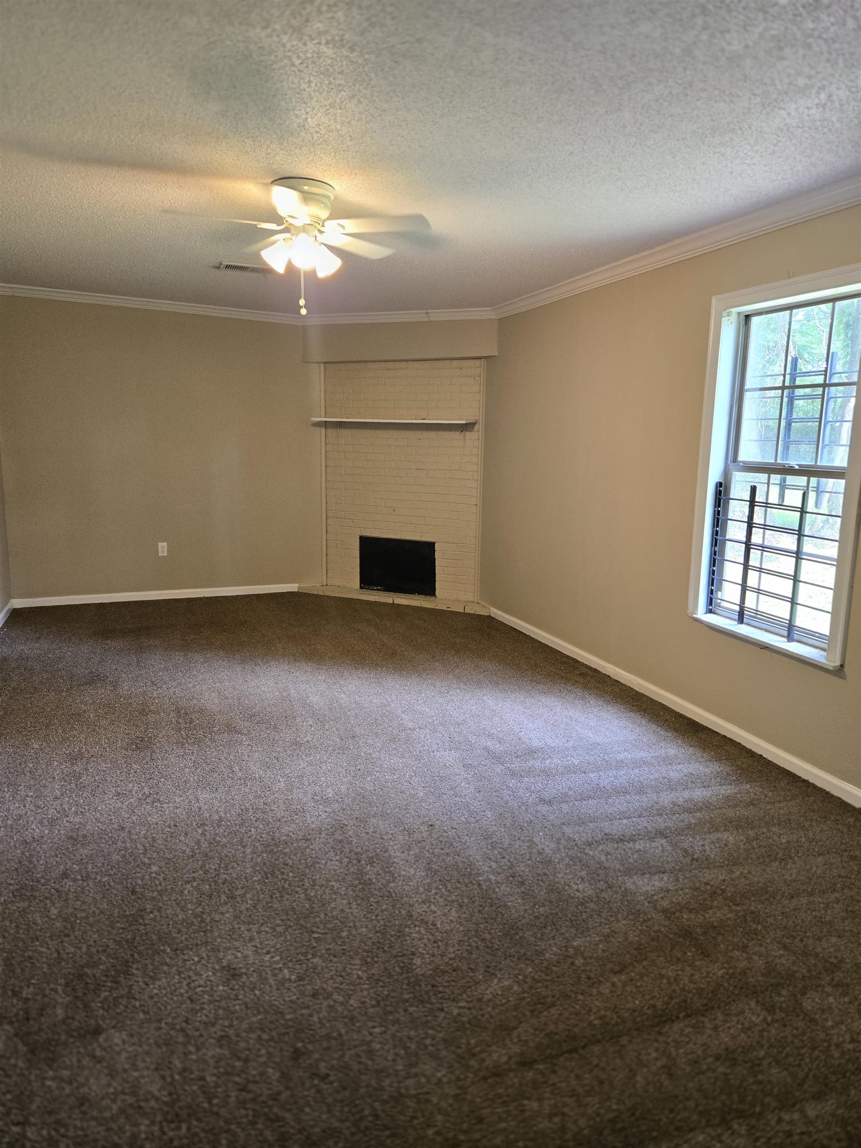 4207 Kenosha Road Memphis, TN 38118 - Photo 17 of 24 Unfurnished living room featuring a textured ceiling, crown molding, ceiling fan, dark colored carpet, and a fireplace
