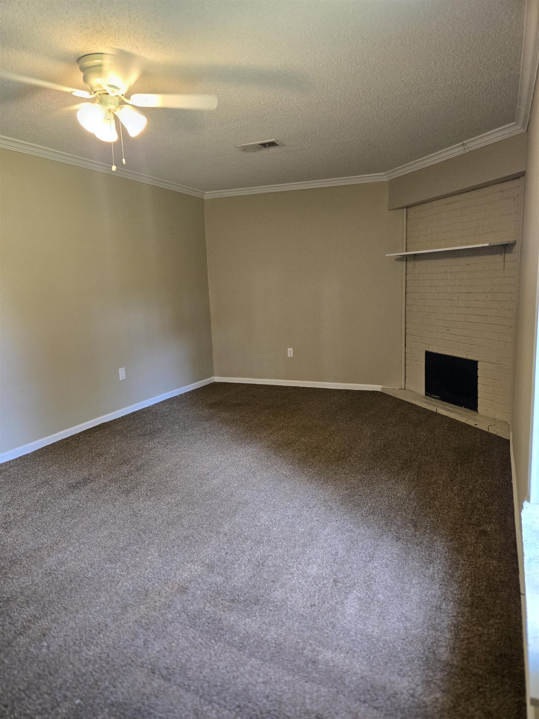 4207 Kenosha Road Memphis, TN 38118 - Photo 19 of 24 Unfurnished living room featuring a textured ceiling, ornamental molding, a ceiling fan, carpet floors, and a fireplace