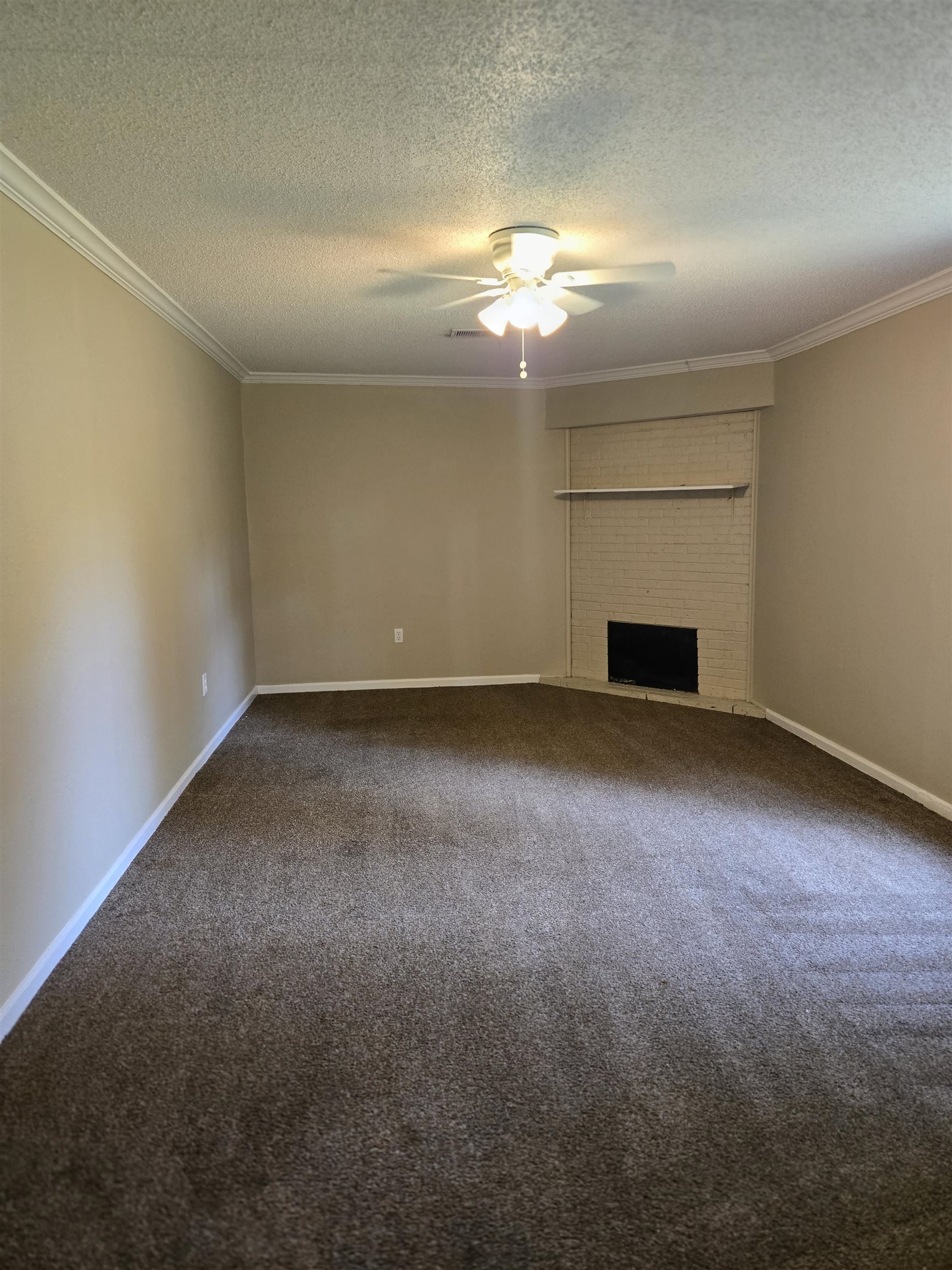 4207 Kenosha Road Memphis, TN 38118 - Photo 10 of 24 Unfurnished living room with ceiling fan, a textured ceiling, dark carpet, crown molding, and a brick fireplace