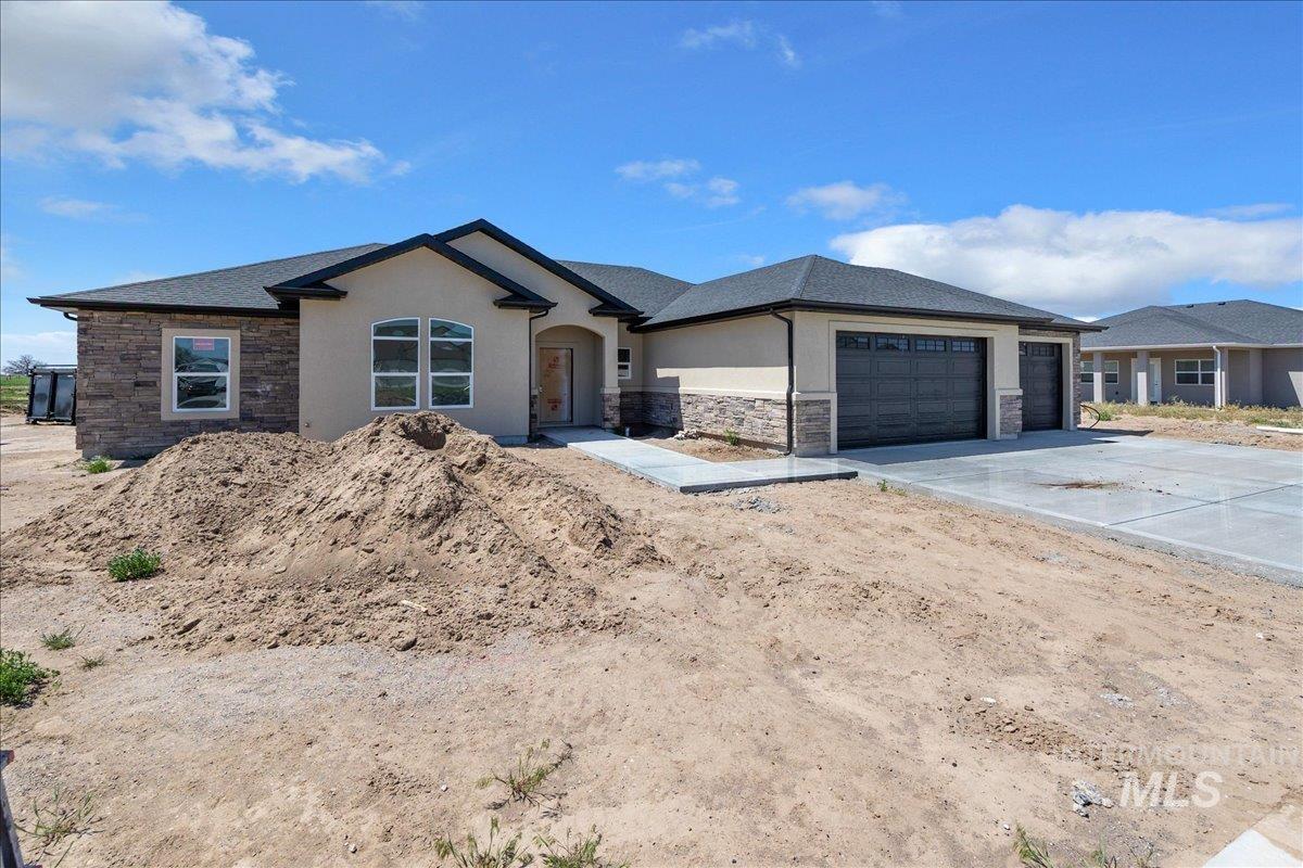 1205 Moss Rupert, ID 83350 - Photo 2 of 3 Single-story residence featuring a stucco and stone veneer exterior, a dark shingle roof, and a two-car garage with paneled doors