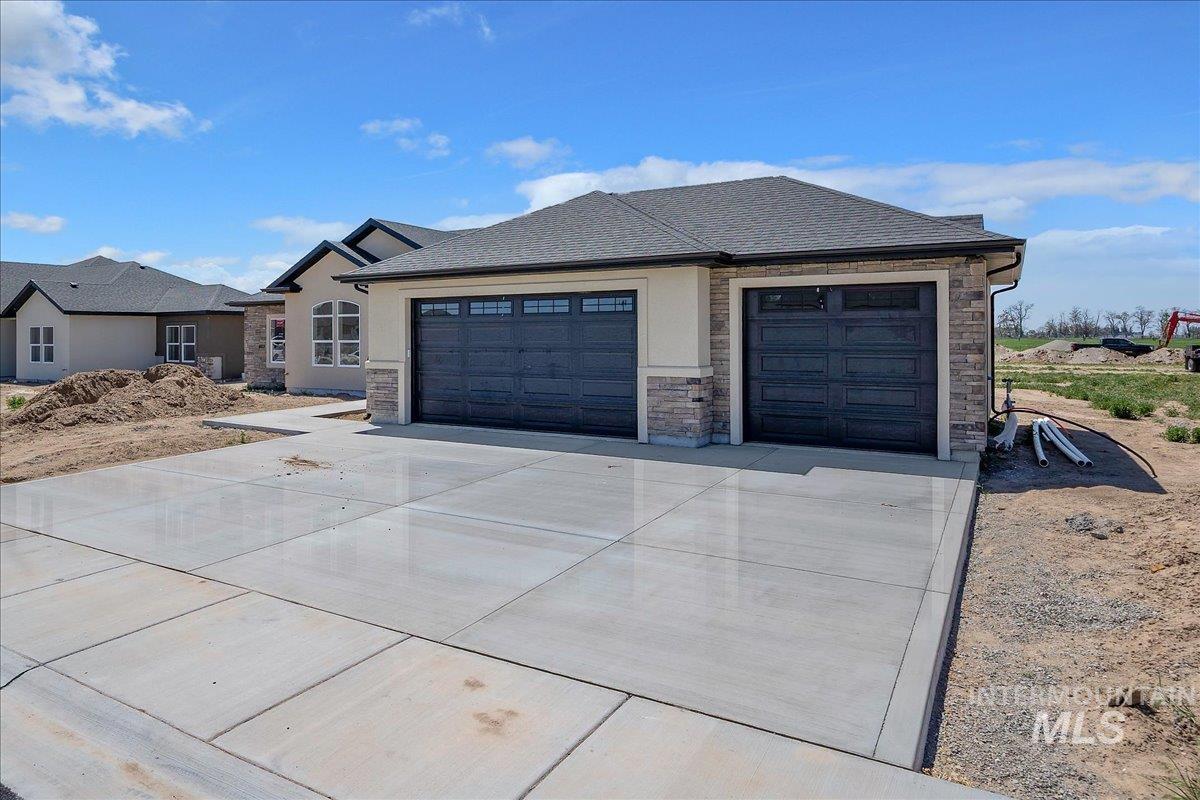 1205 Moss Rupert, ID 83350 - Photo 3 of 3 Exterior featuring a multi-car concrete driveway, stone accents, stucco siding, dark garage doors with window inserts, and a dark shingle roof
