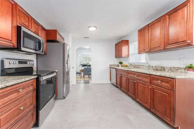 a kitchen with stainless steel appliances granite countertop a stove top oven a sink dishwasher and a refrigerator with wooden cabinets