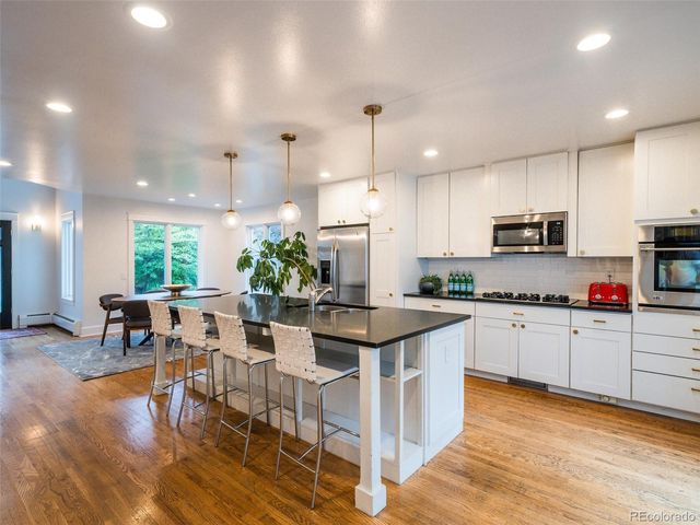 a kitchen with stainless steel appliances granite countertop a stove top oven a sink dishwasher a dining table and chairs with wooden floor