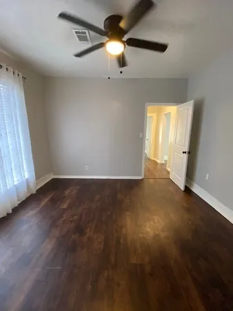an empty room with wooden floor chandelier fan and windows