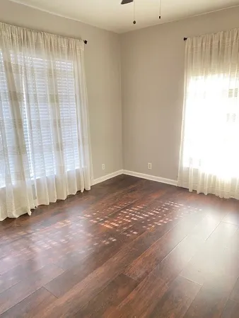 an empty room with wooden floor and windows with curtains