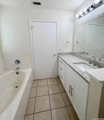 a spacious bathroom with a granite countertop sink a mirror and a bathtub
