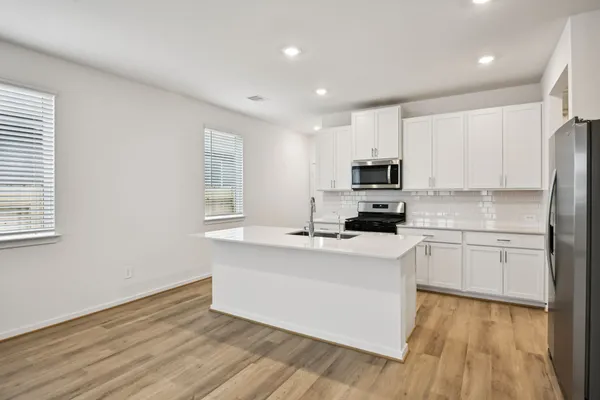 a kitchen with stainless steel appliances granite countertop a stove top oven a sink a refrigerator and white cabinets with wooden floor