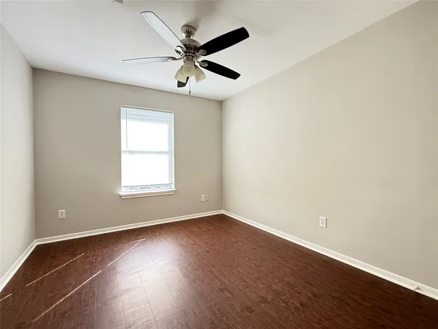 an empty room with wooden floor ceiling fan and windows
