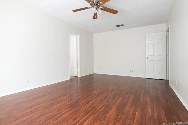 an empty room with wooden floor fan and windows