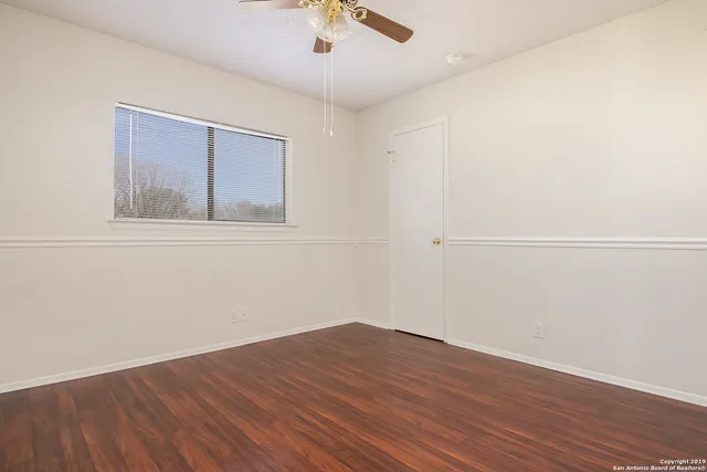 an empty room with wooden floor fan and windows