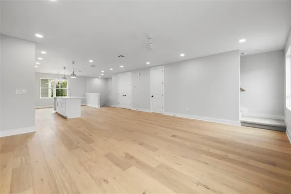 a view of an empty room with wooden floor and a kitchen