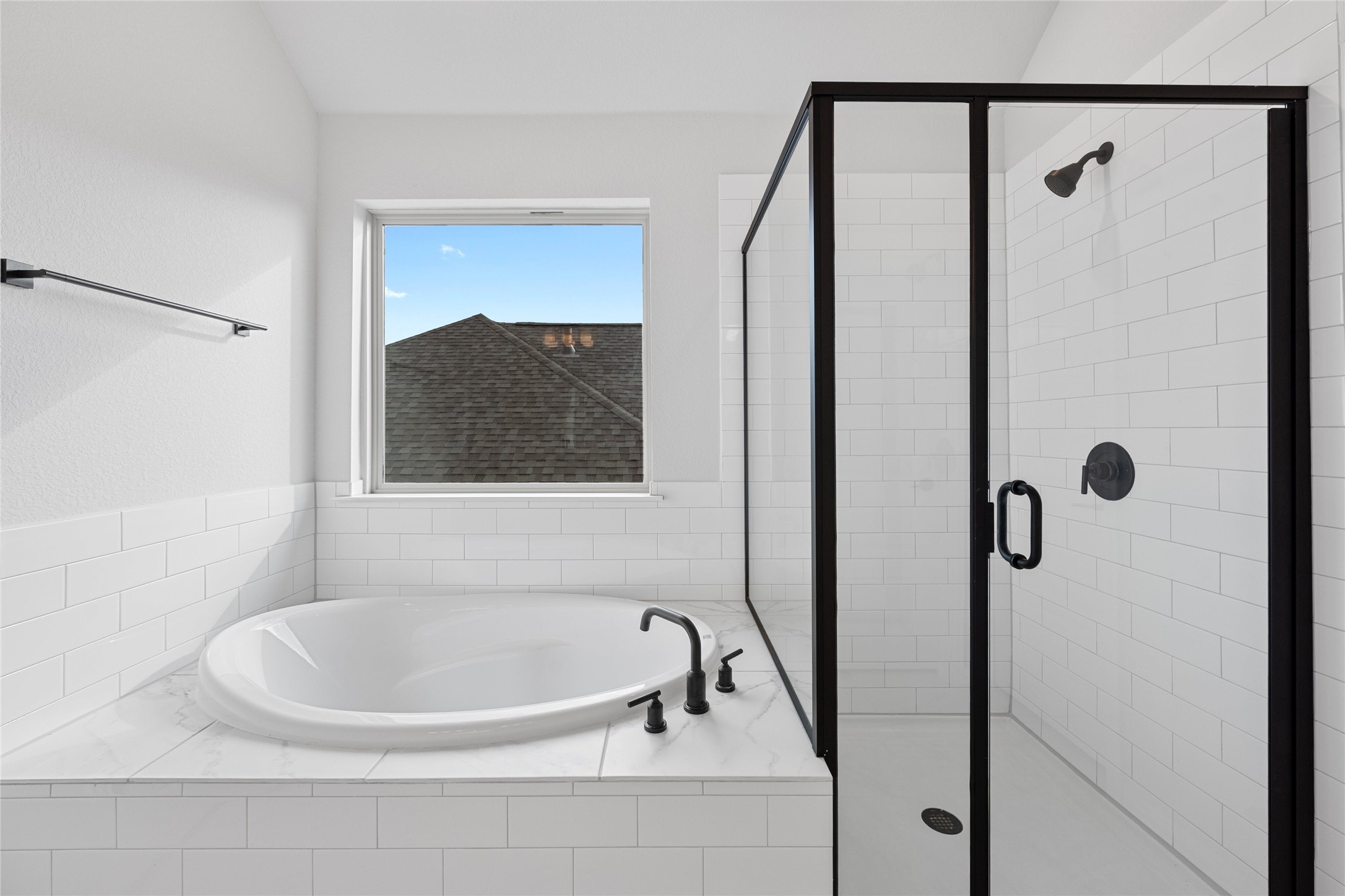 303 Fawn Riv Run Kyle, TX 78640 - Photo 18 of 32 Soaking tub with black fixtures, subway tile surround, and a separate glass-enclosed shower featuring a black frame and hardware