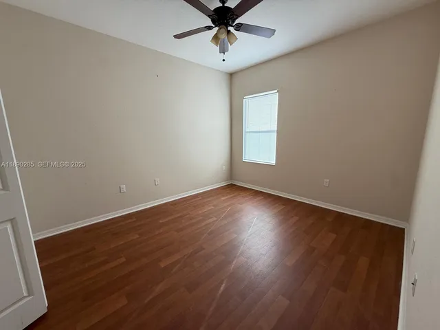 an empty room with wooden floor fan and windows