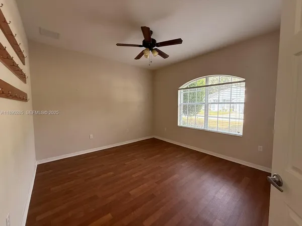 an empty room with wooden floor ceiling fan and windows