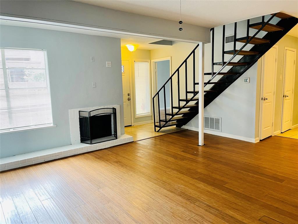 3121 Park Lane, Unit 1105 Dallas, TX 75220 - Photo 5 of 19 Unfurnished living room featuring wood finished floors, healthy amount of natural light, stairs, and a fireplace with raised hearth