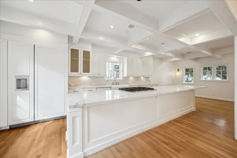 a large white kitchen with kitchen island a sink wooden floor and stainless steel appliances