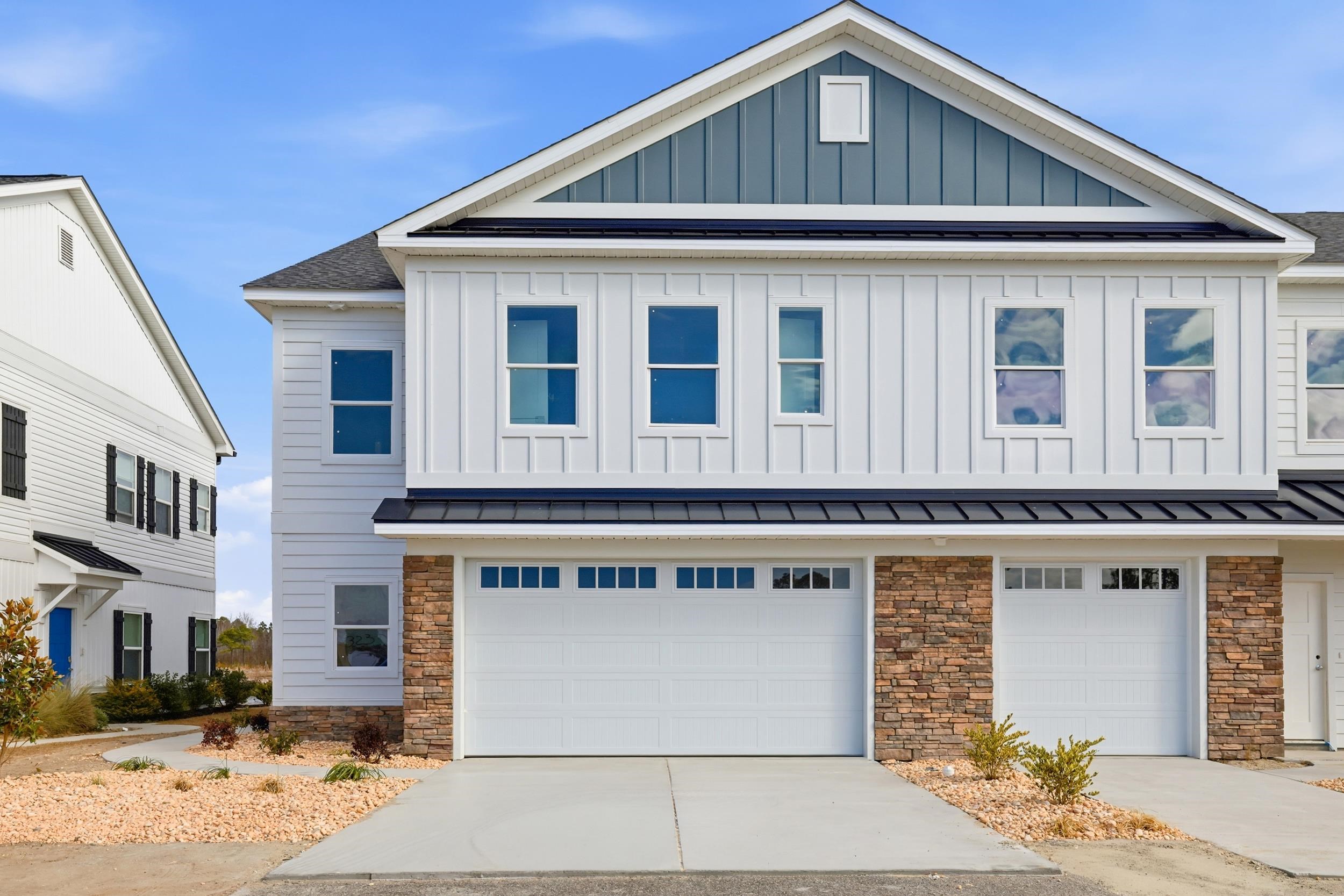 View of front of home with stone siding, a standing seam roof, board and batten siding, driveway, and an attached garage