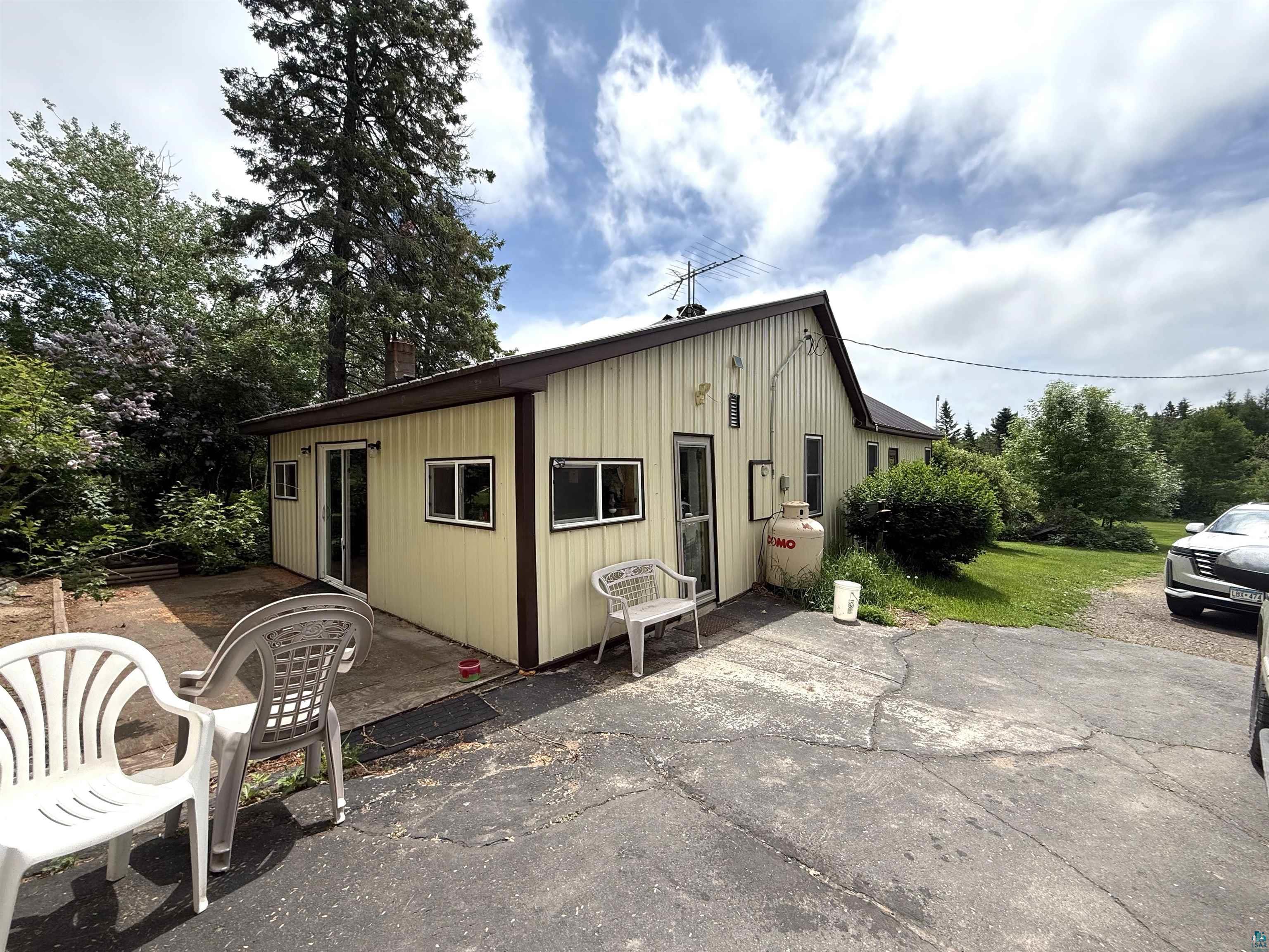 3541 Bent Trout Lake Road Barnum, MN 55707 - Photo 35 of 41 Exterior featuring light yellow vertical siding with dark trim, multiple windows providing natural light, a side patio area, and a large propane tank