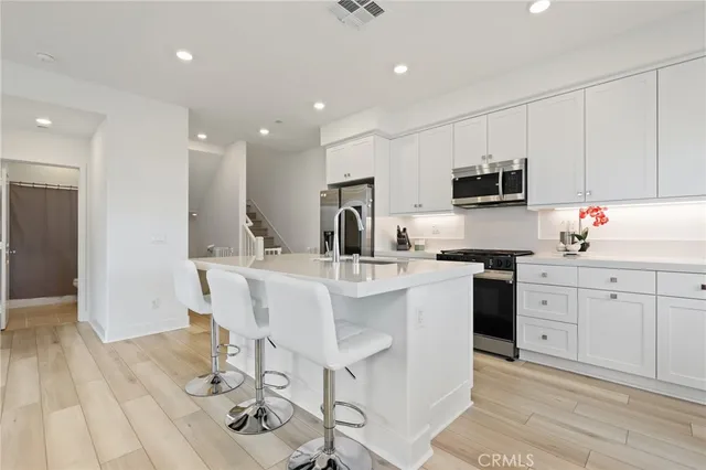 a kitchen with stainless steel appliances a sink a stove a refrigerator with white cabinets and wooden floor