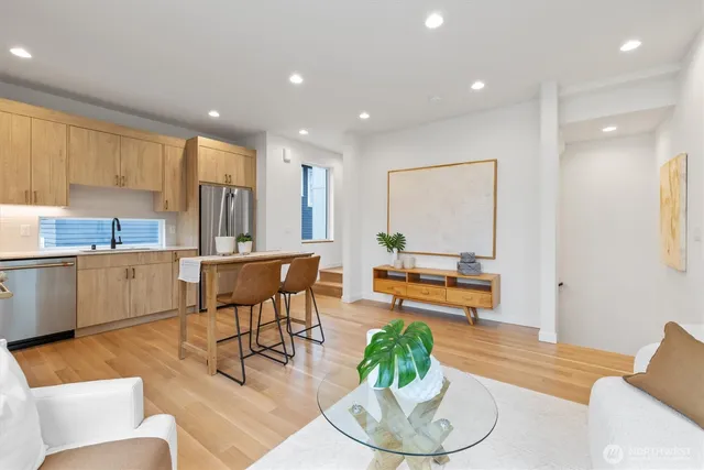 a living room with kitchen couches kitchen view and a large window