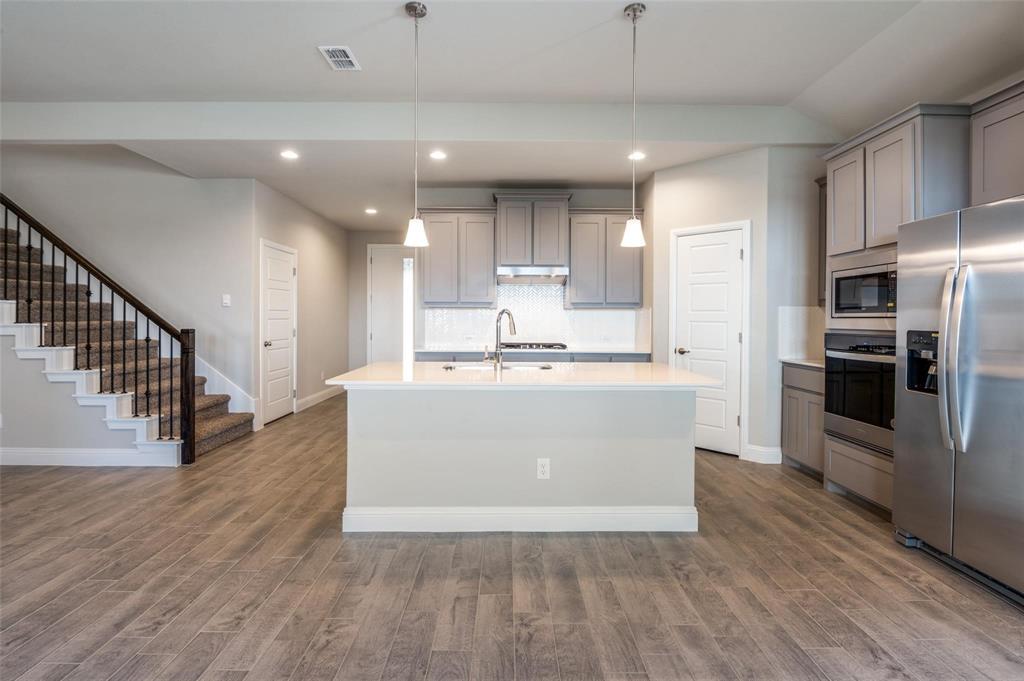 1517 Razorbill Road Denton, TX 76205 - Photo 4 of 25 Kitchen island with sink, stainless steel appliances, wood-finish flooring, recessed lighting, and a staircase with metal balusters