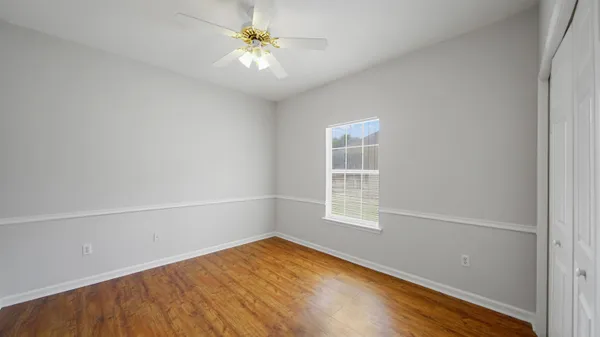 an empty room with wooden floor fan and windows