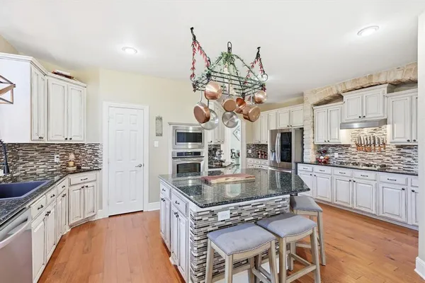 a kitchen with stainless steel appliances granite countertop a stove top oven a sink dishwasher and white cabinets with wooden floor