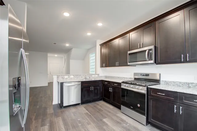 a kitchen with stainless steel appliances granite countertop a stove a sink dishwasher a refrigerator and a microwave oven with wooden floor