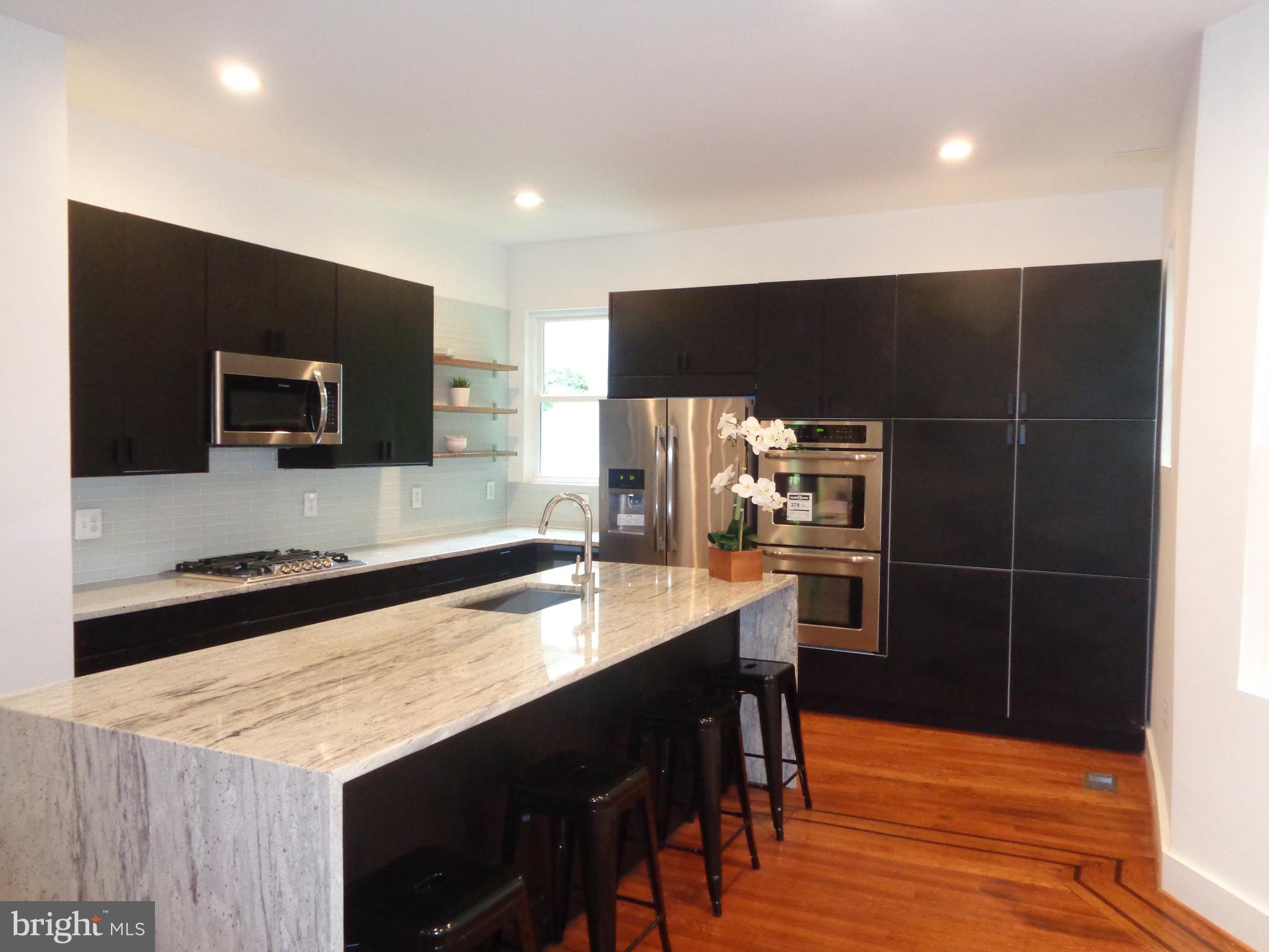 5105 Roland Avenue Baltimore, MD 21210 - Photo 5 of 19 a kitchen with stainless steel appliances a kitchen island hardwood floor sink and stove