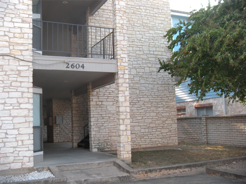 View of exterior entry with stone siding, a balcony, and fence