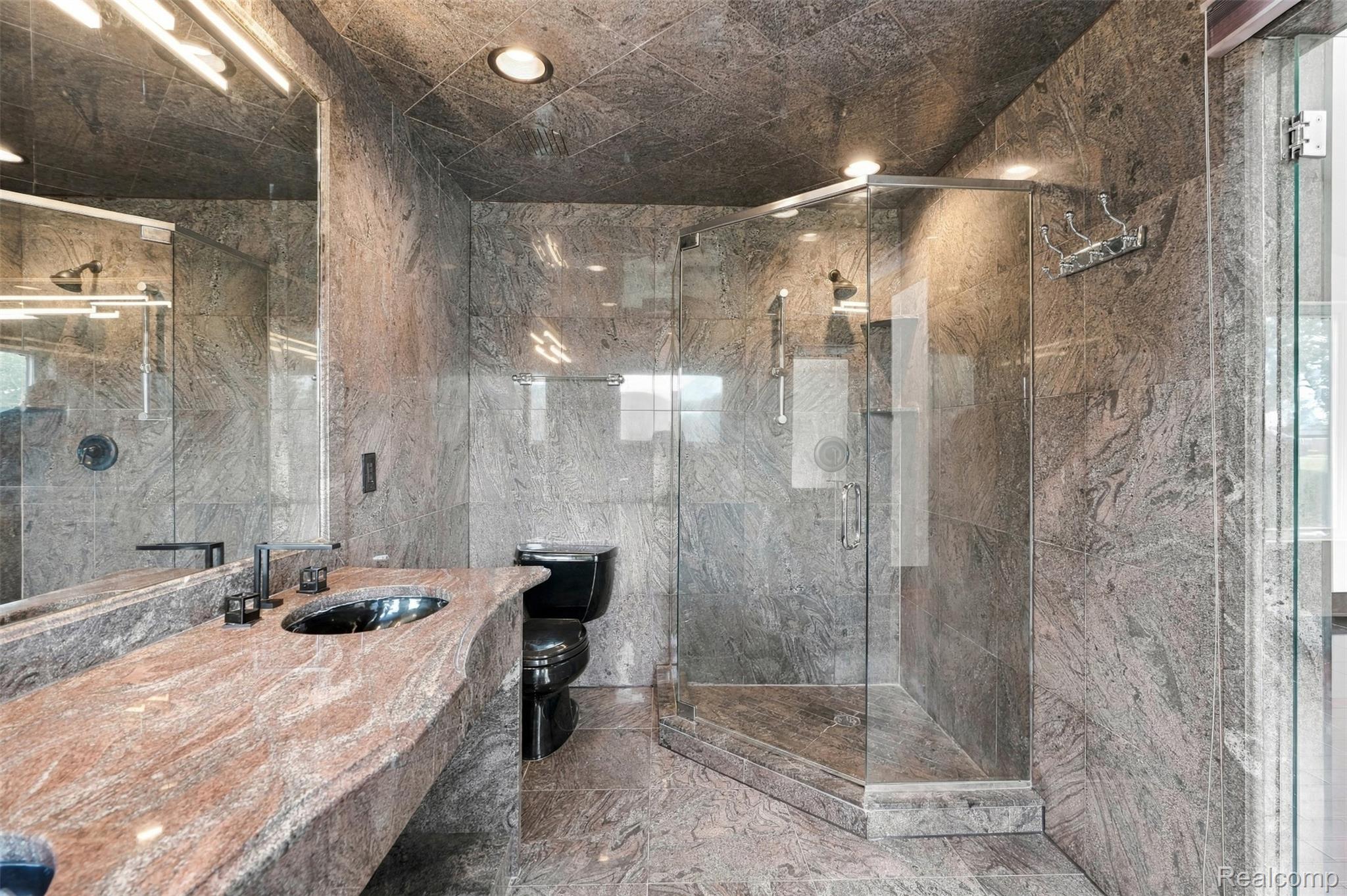 27507 Bell Road Southfield, MI 48034 - Photo 36 of 81 Bathroom featuring a glass-enclosed shower, stone-finish walls, stone-finish flooring, a black toilet, and a vanity with an integrated sink