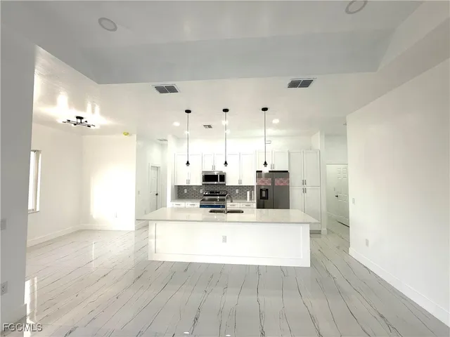 a large white kitchen with granite countertop a large counter top stainless steel appliances and cabinets