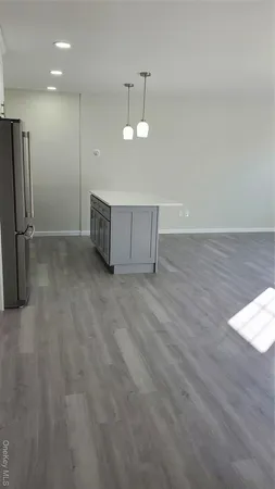 an empty room with wooden floor kitchen view and a refrigerator